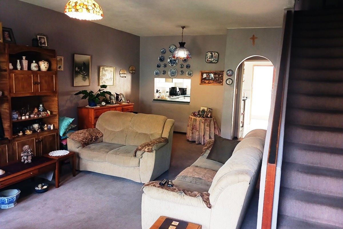 A spacious living room featuring a staircase, an arched doorway, and a pass-through window connecting to the kitchen area.