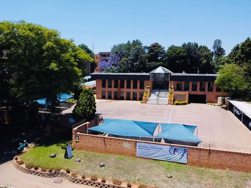 Aerial view of a commercial property featuring a brick building, paved parking area with shade cloth carports, and a perimeter wall.