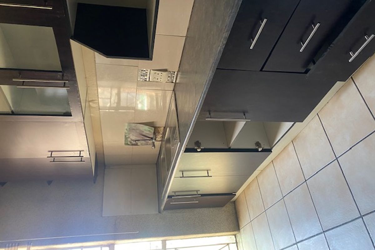 A functional kitchen featuring dark cabinetry, laminate countertops, and a stainless steel sink, requiring some maintenance and cosmetic updates.