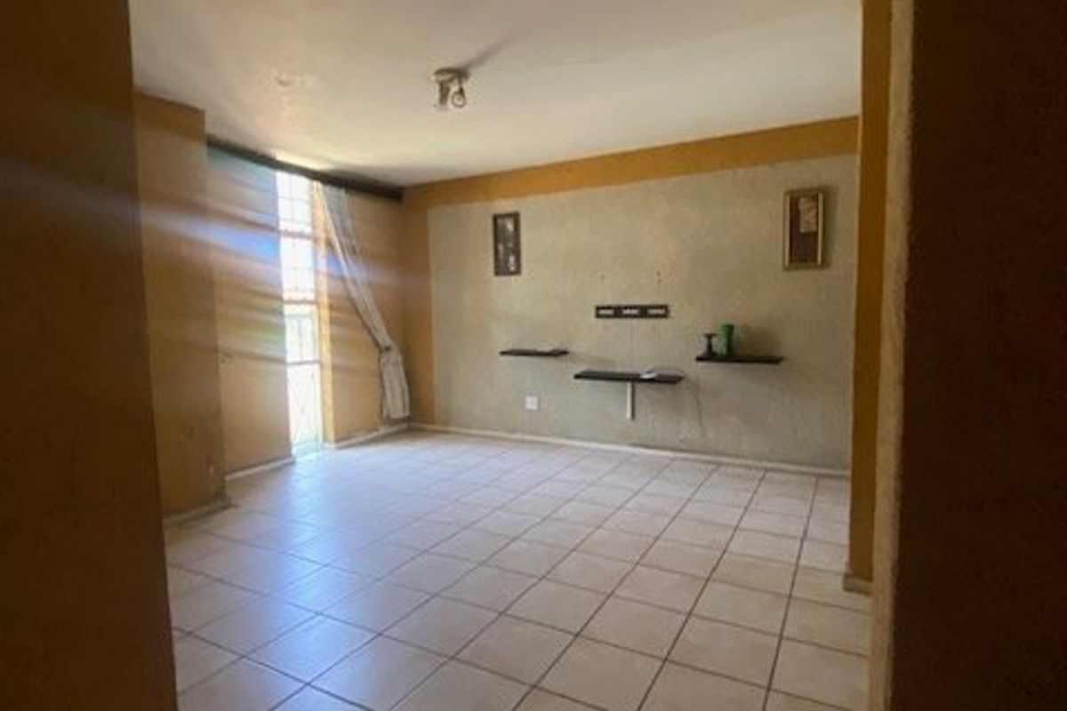 An empty living room featuring ceramic floor tiles, built-in wall shelving, and natural light from a large window.