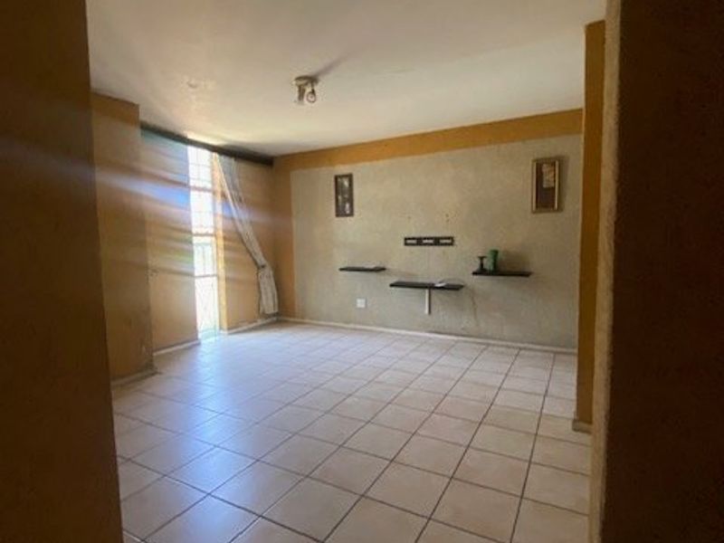 An empty living room featuring ceramic floor tiles, built-in wall shelving, and natural light from a large window.