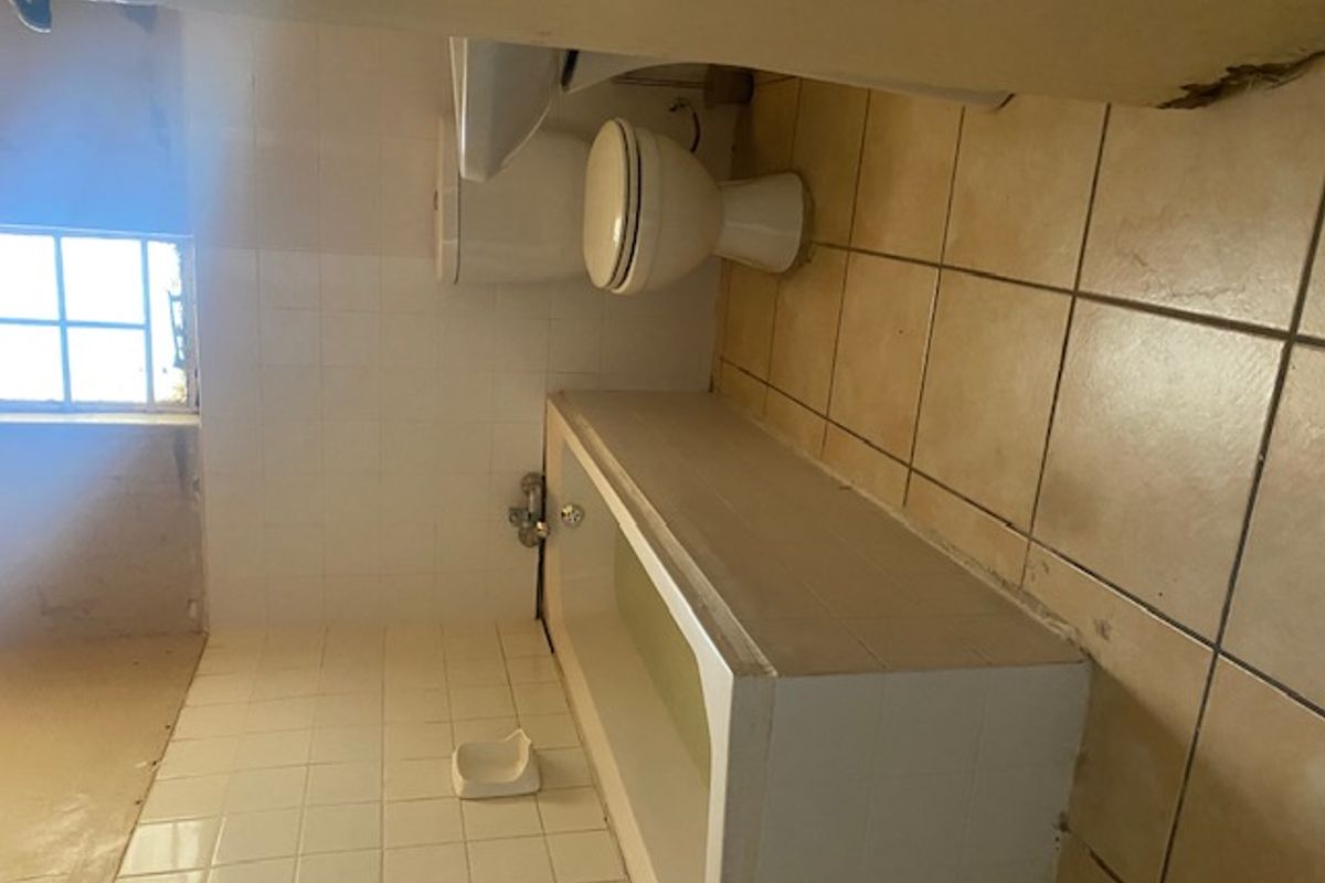 A dated bathroom featuring a bathtub, toilet, and pedestal basin, requiring renovation to address damaged wall finishes and worn tiling.