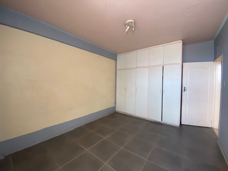 An empty bedroom featuring tiled flooring and built-in cupboards, offering a blank canvas for potential renovation or staging.