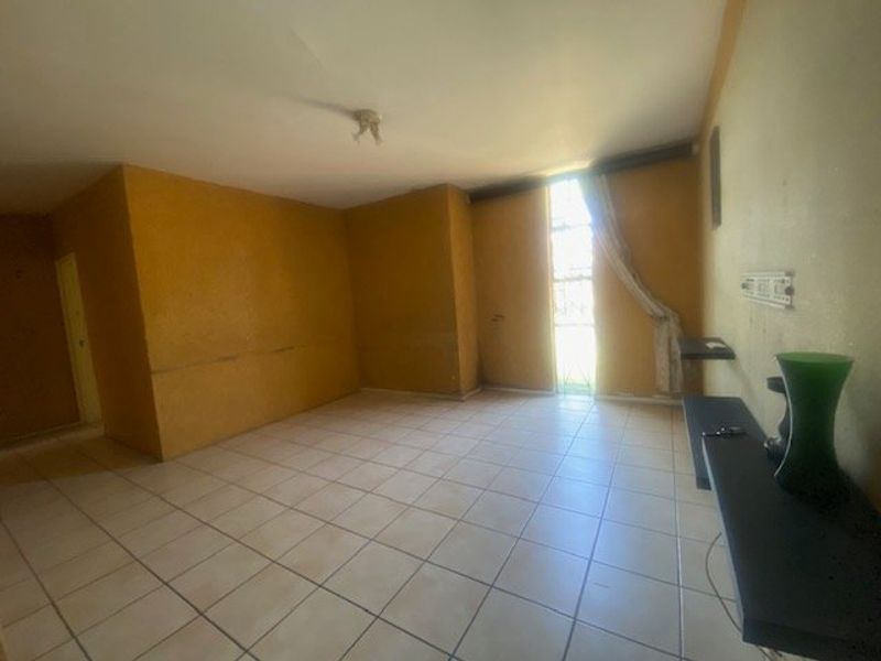 An empty living room featuring tiled flooring and built-in wall shelving, requiring cosmetic updates to the walls and ceiling.