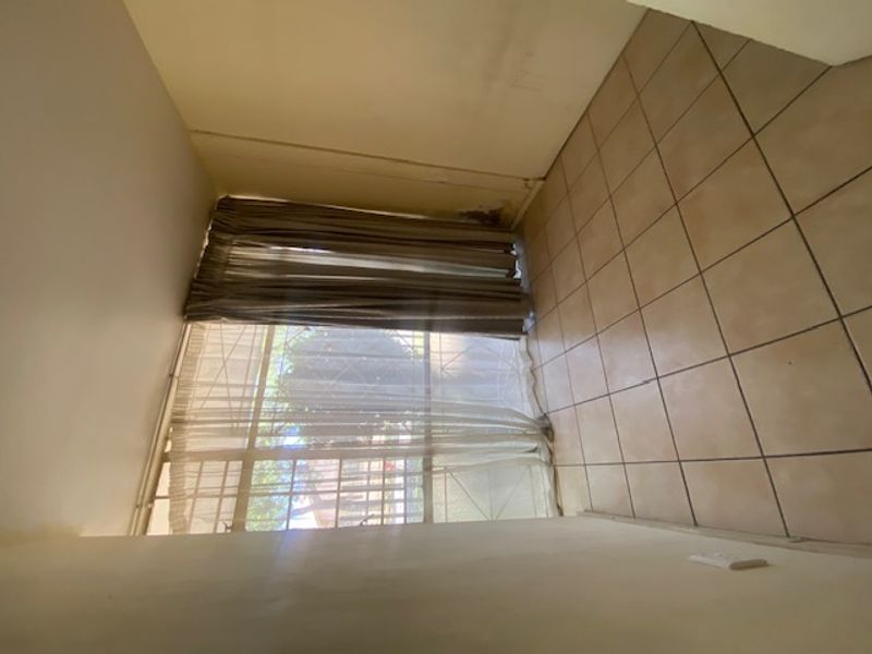 An empty living area featuring tiled flooring and a large window with security bars, requiring cosmetic updates to the walls.