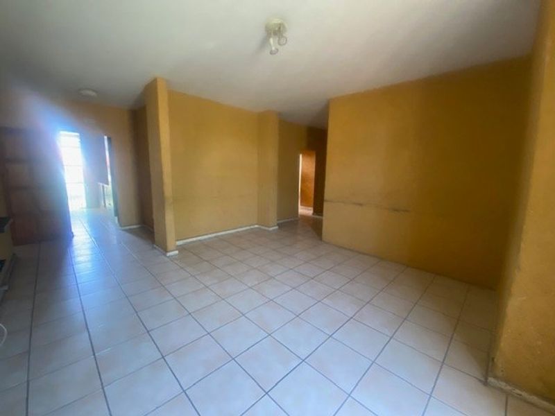 An empty, open-plan living area featuring ceramic floor tiles and neutral wall finishes, offering a blank canvas for renovation and interior design.