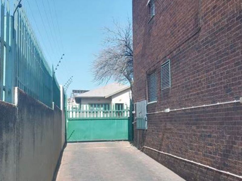 A view of the rear access driveway featuring a brick boundary wall with electric fencing and a secure metal gate.