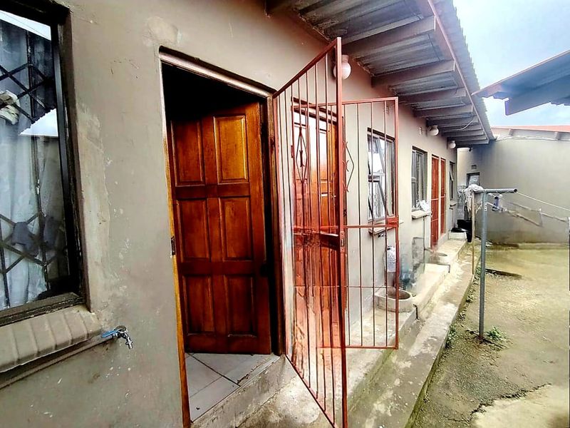 Rear exterior view of the apartment featuring a security gate, timber door, and external water tap along a concrete pathway.