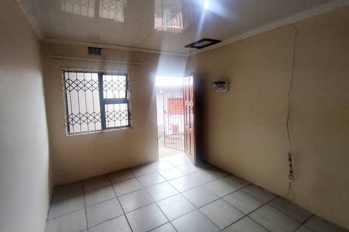 An empty living area featuring tiled flooring, security bars on the window, and direct access to an outdoor space.