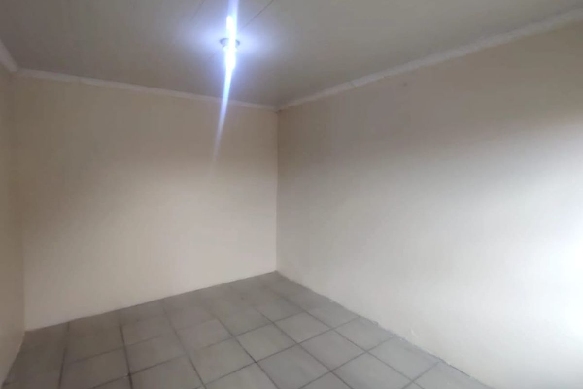 An empty, neutral-toned bedroom featuring tiled flooring and a simple ceiling light fixture, providing a blank canvas for personalization.