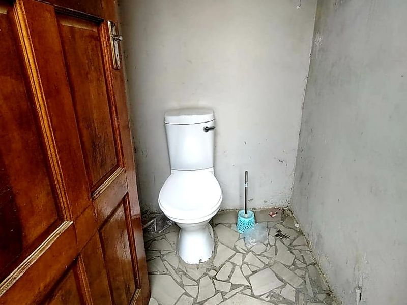 A small, unfinished bathroom featuring a toilet, stone tile flooring, and a wooden door, requiring significant cosmetic updates and finishing.