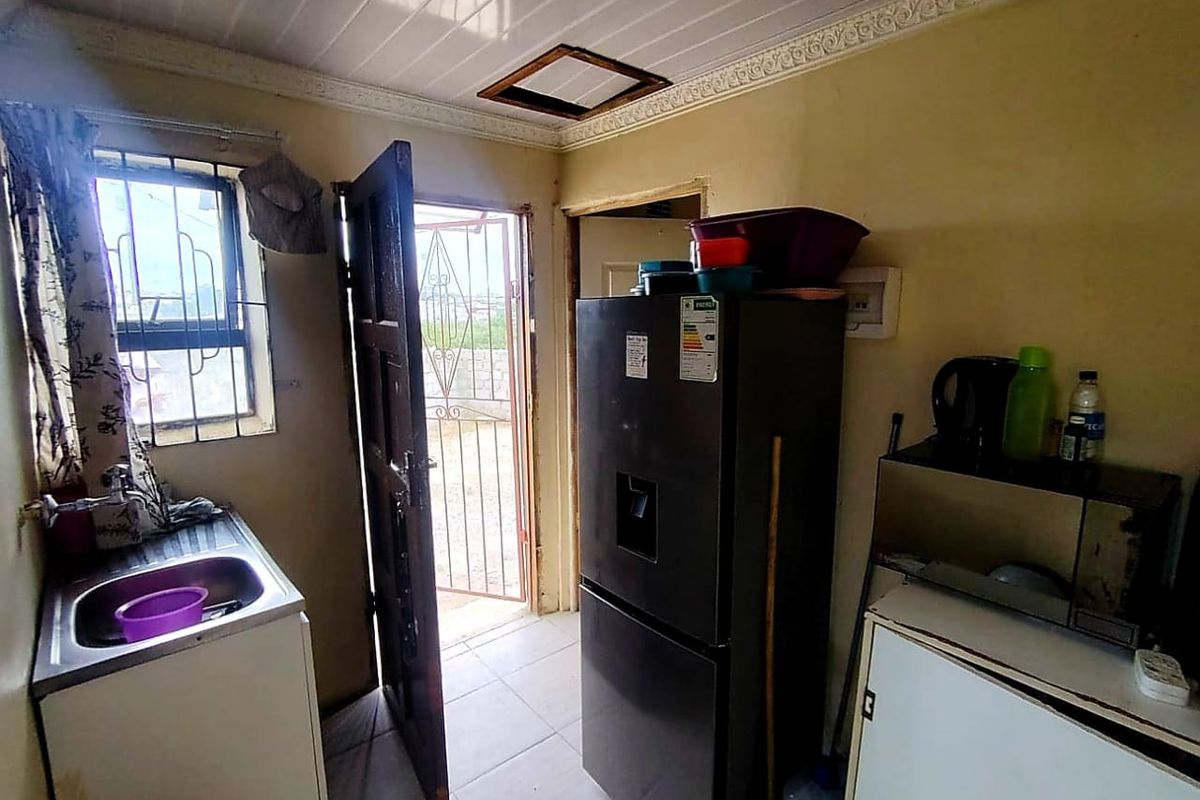 A compact kitchen area featuring a stainless steel sink, tiled flooring, and direct access to an exterior security gate.