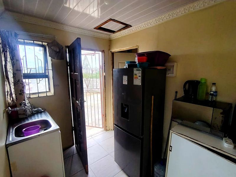 A compact kitchen area featuring a stainless steel sink, tiled flooring, and direct access to an exterior security gate.