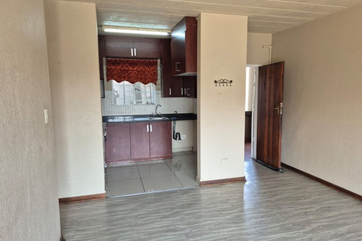 Open plan living area featuring a compact kitchen with built-in cabinetry, tiled flooring, and laminate wood-look flooring in the main living space.