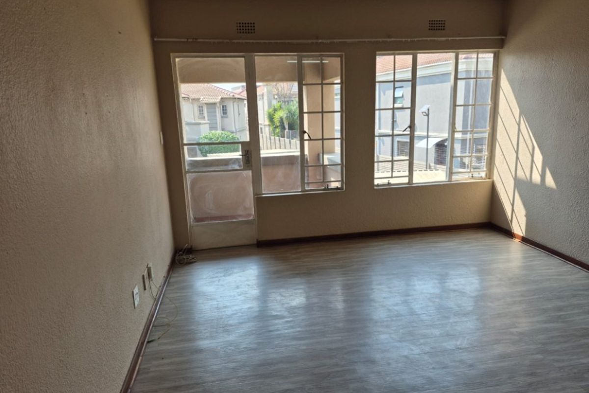 An empty living room featuring laminate flooring, large windows, and a glass panel door leading to an outdoor area.