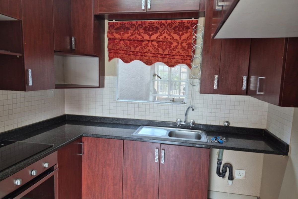 A functional kitchen featuring dark wood cabinetry, granite countertops, a tiled backsplash, and built-in oven and hob, with an integrated sink area.