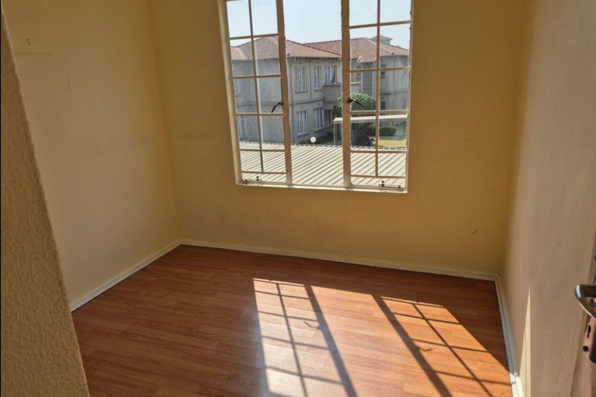 An empty bedroom featuring laminate flooring and a window with security bars, offering a blank canvas for personalization.