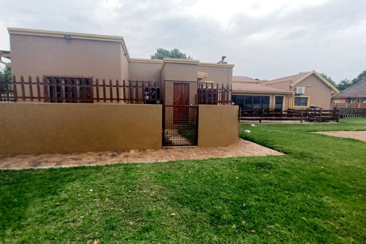 Rear view of the property featuring a paved patio area, security gate, and a spacious lawn with established perimeter fencing.