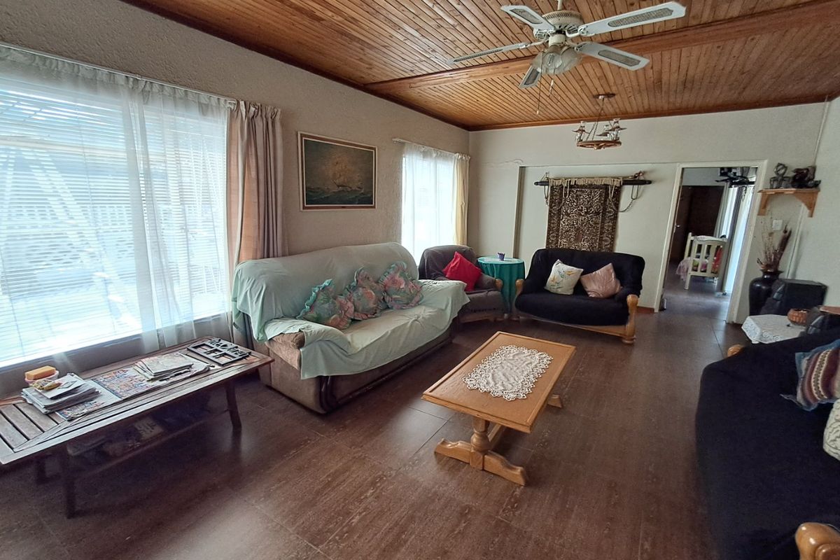 A spacious living room featuring a timber tongue and groove ceiling, ceiling fan, and tiled flooring, offering a comfortable and functional living space.