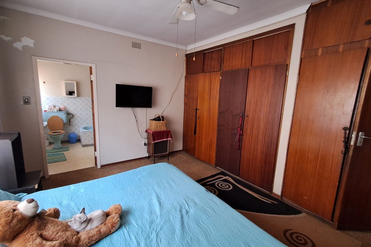 A bedroom featuring built-in wooden cupboards, a ceiling fan, and carpeted flooring, with an adjoining bathroom visible through the doorway.