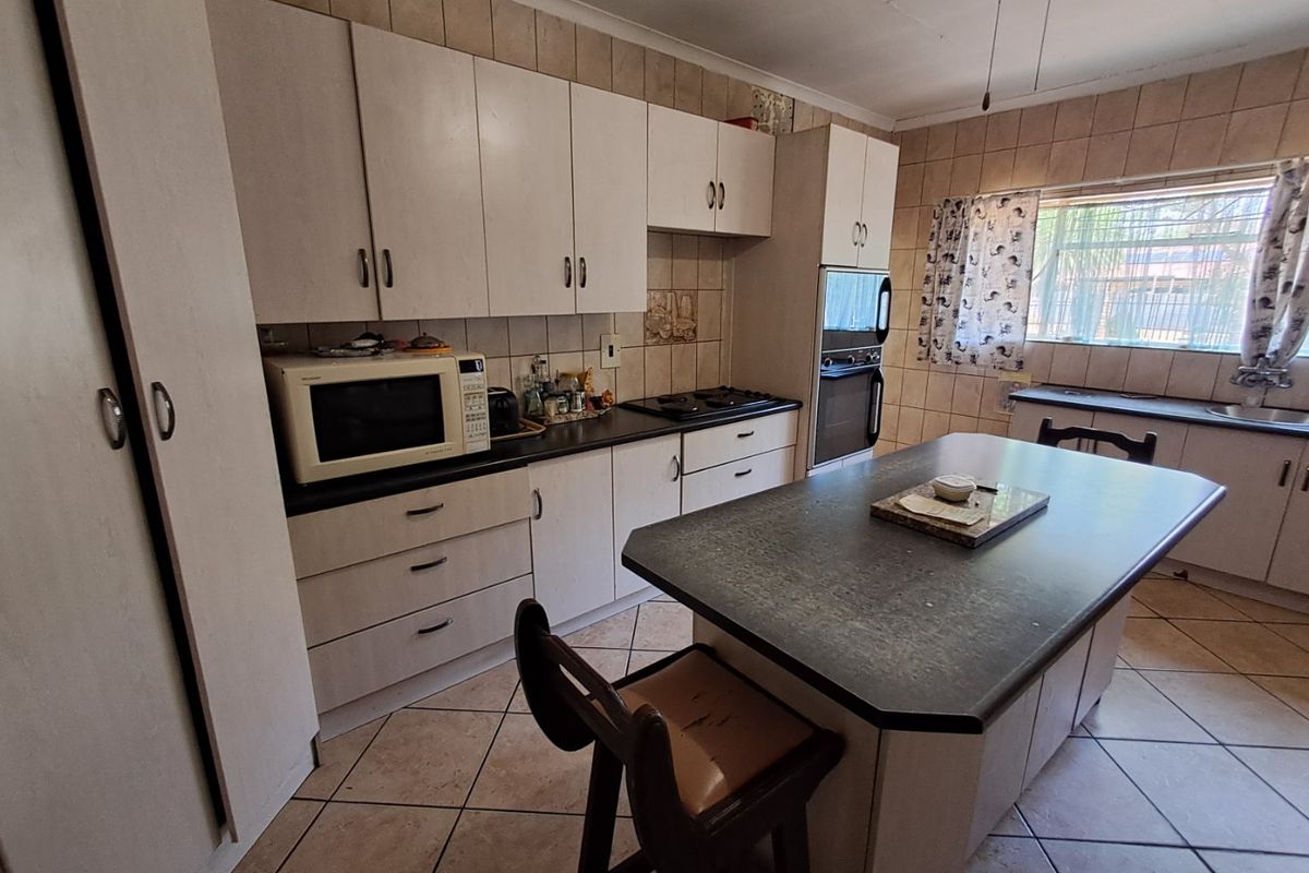 A functional kitchen featuring built-in cabinetry, a central island, integrated oven and hob, and tiled finishes throughout.