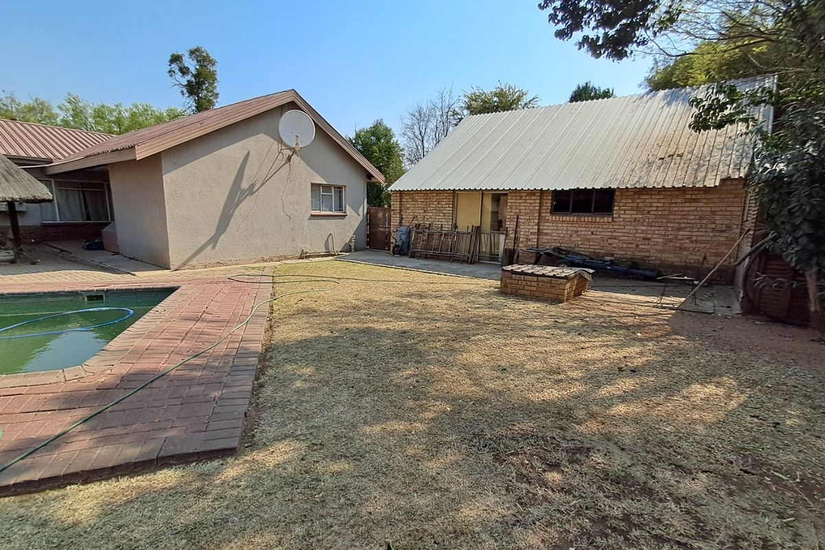 Rear garden area featuring a swimming pool, brick paving, and outbuilding with a corrugated metal roof.