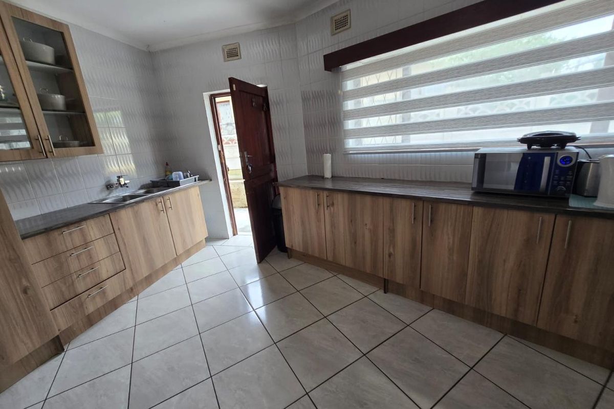 A functional kitchen featuring wood-look laminate cabinetry, dark countertops, tiled walls, and ceramic flooring with direct access to an exterior door.
