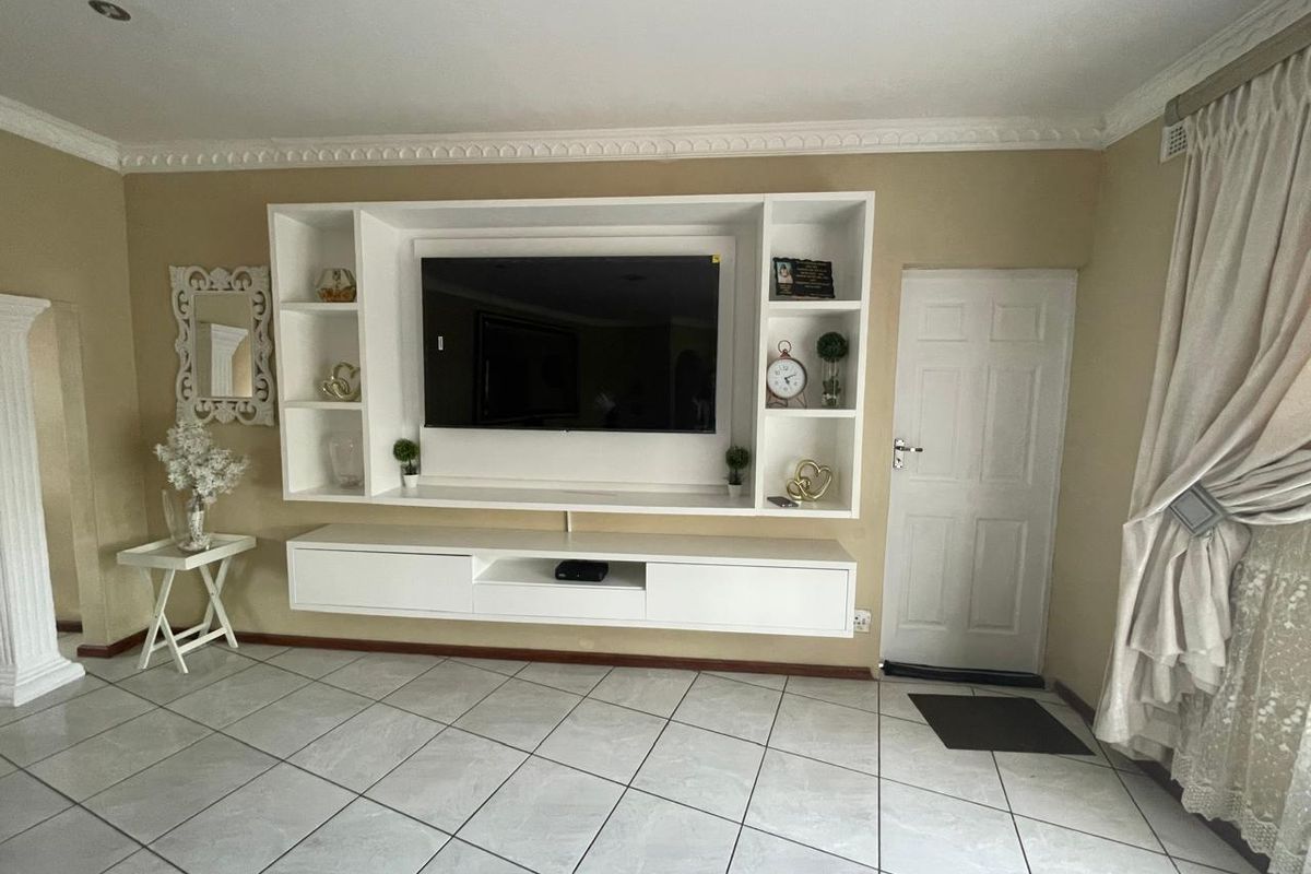A living room featuring a modern white built-in media unit, tiled flooring, and decorative ceiling cornicing.