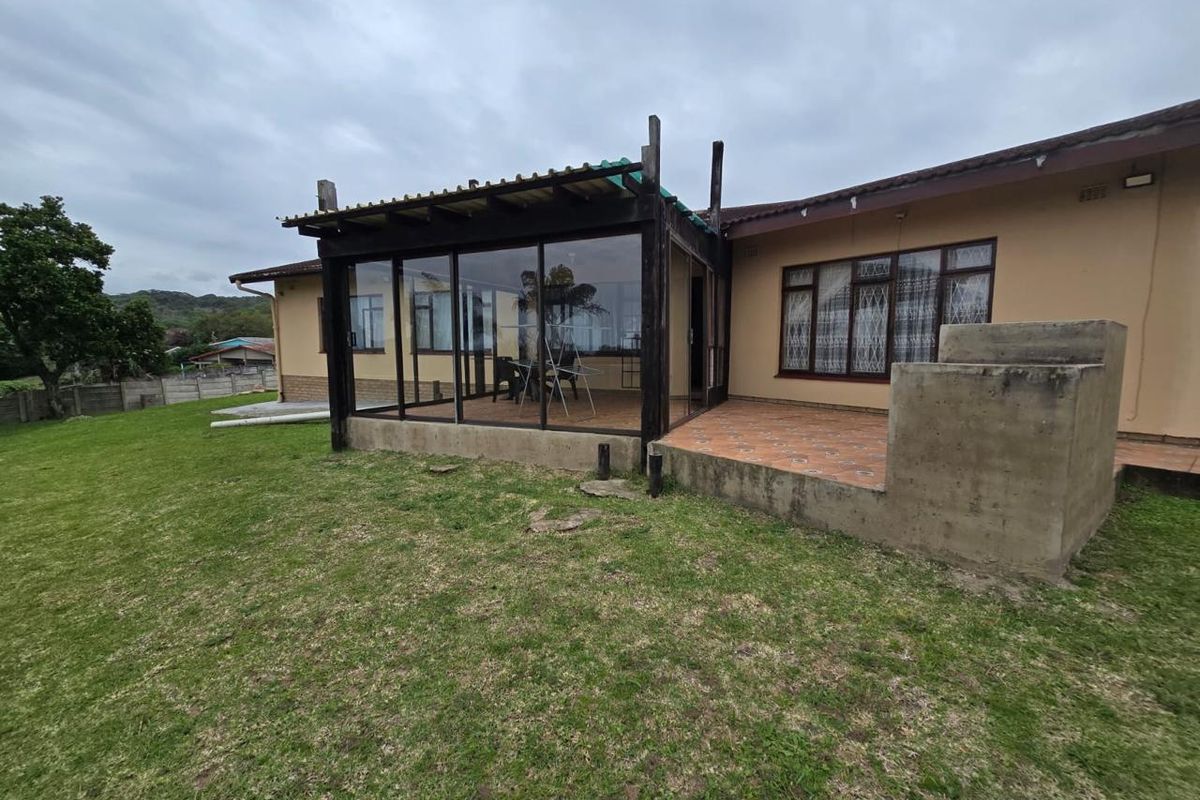 Rear view of the property featuring an enclosed patio area with timber framing, tiled terrace, and a concrete retaining wall overlooking the garden.