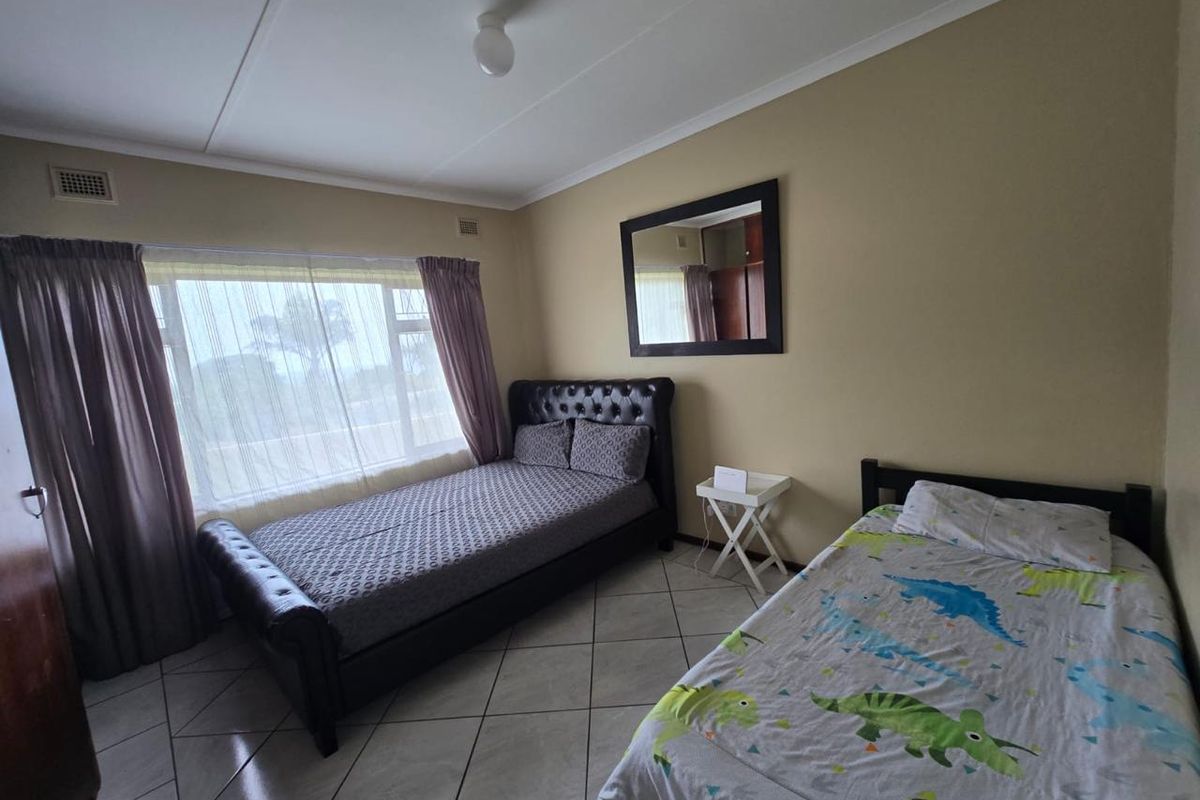 A functional bedroom featuring tiled flooring and a large window, providing a comfortable space with neutral wall tones.