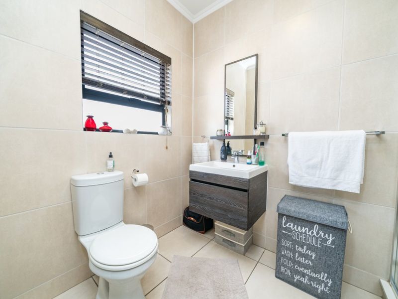 A modern, well-maintained bathroom featuring neutral ceramic tiling, a wall-mounted vanity unit, and a clean, functional layout.
