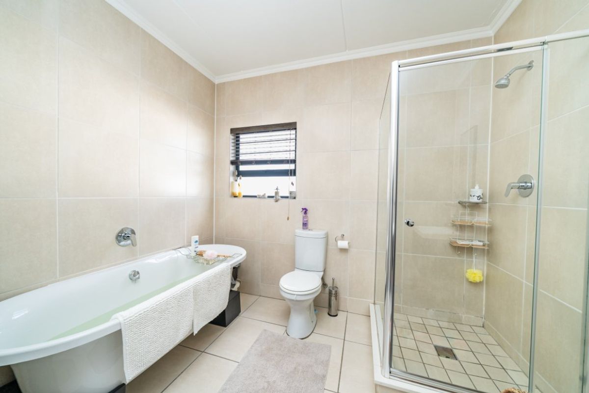 A well-maintained bathroom featuring a freestanding bathtub, a separate glass-enclosed shower, and neutral floor-to-ceiling wall tiling.