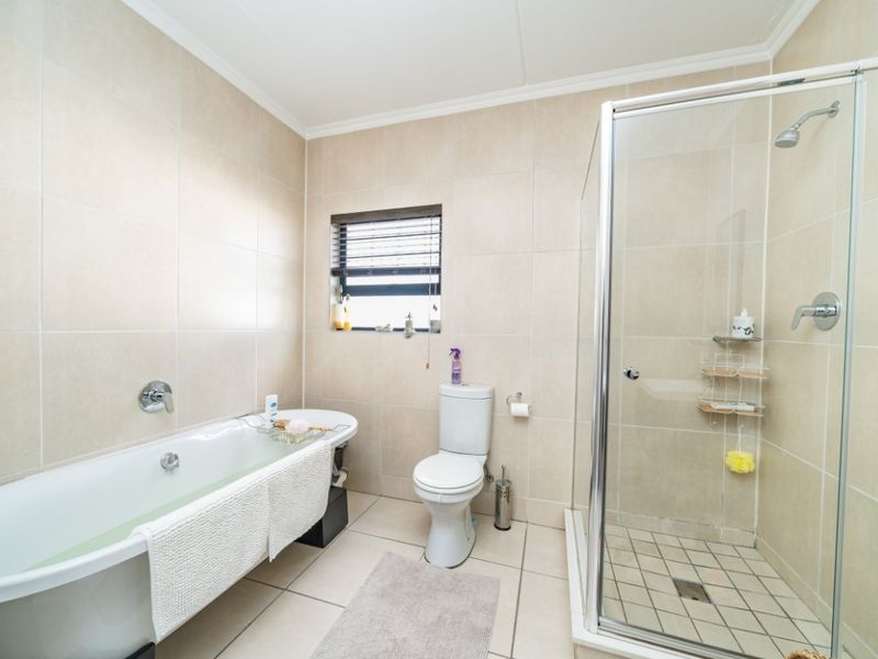 A well-maintained bathroom featuring a freestanding bathtub, a separate glass-enclosed shower, and neutral floor-to-ceiling wall tiling.