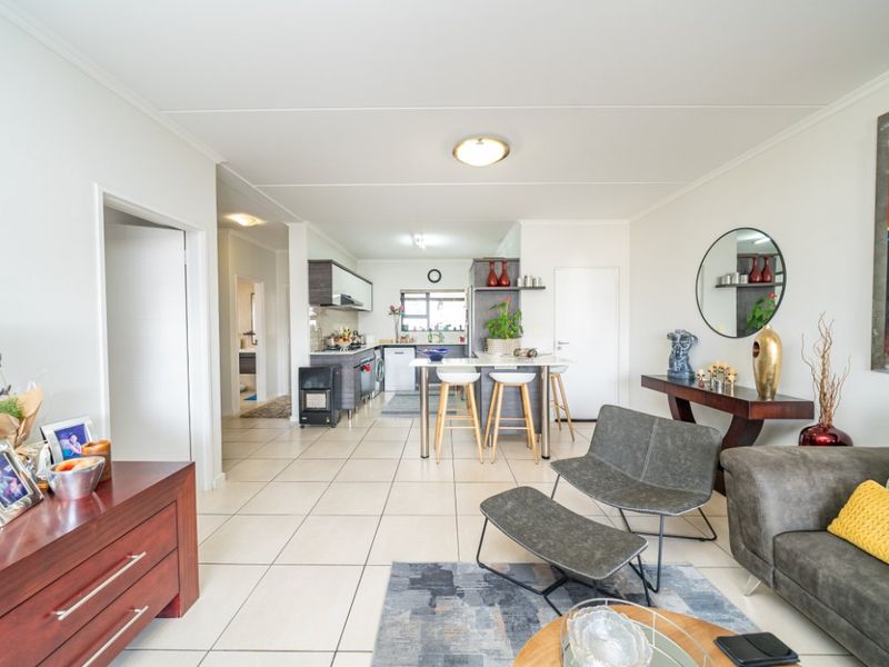 An open-plan living and kitchen area featuring tiled flooring, a central kitchen island, and functional cabinetry, creating a bright and cohesive living space.