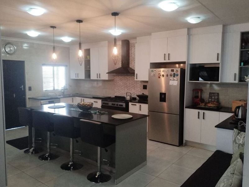 Modern kitchen featuring a central island with breakfast bar, sleek white cabinetry, dark countertops, and integrated stainless steel appliances.