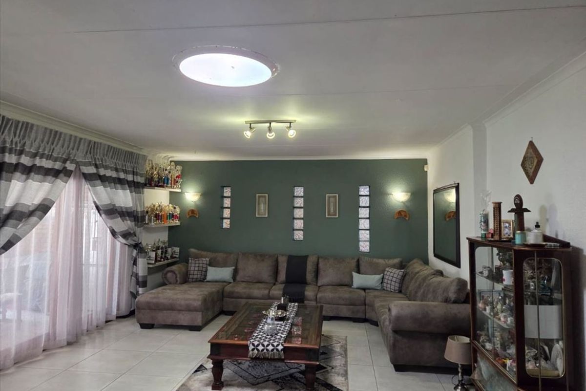 A spacious living room featuring tiled flooring, a green accent wall with decorative glass block inserts, and recessed ceiling lighting.
