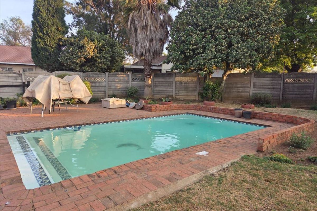 A backyard pool area featuring a rectangular swimming pool with brick paving surround and a concrete boundary wall.