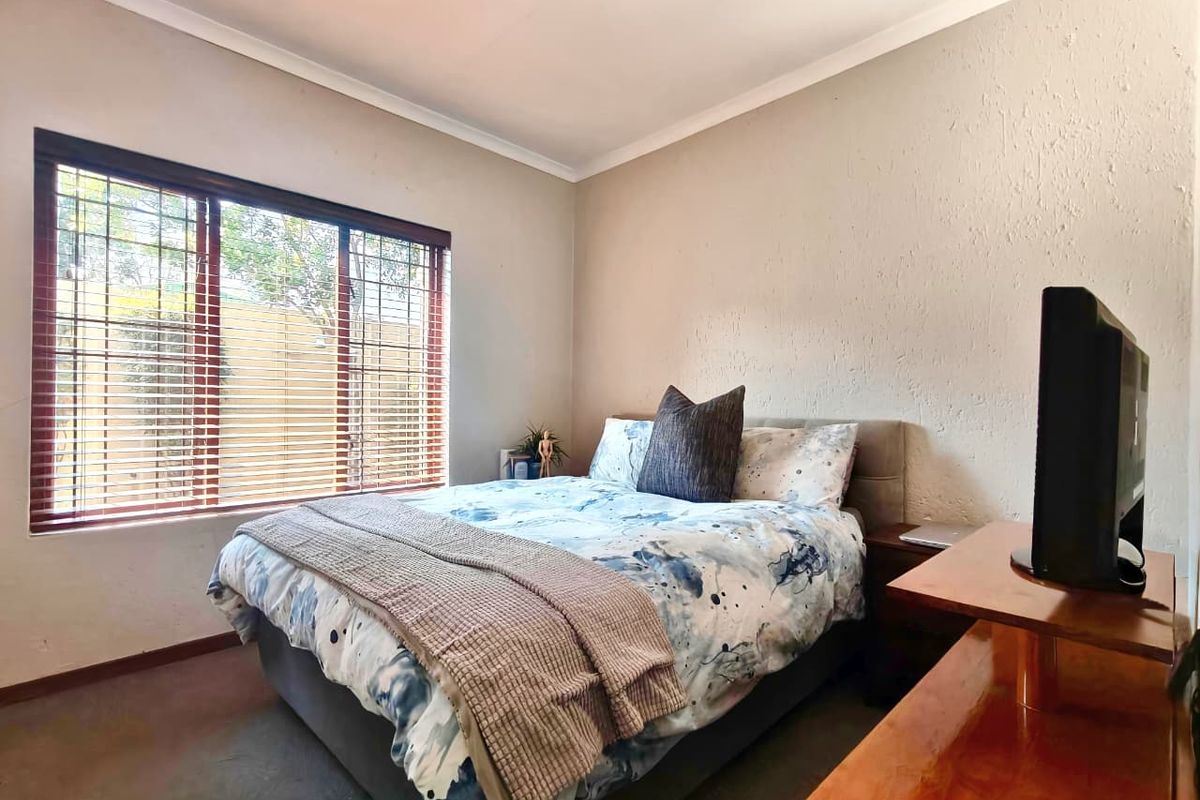 A cozy bedroom featuring a large window with fitted blinds, textured walls, and carpeted flooring, providing a comfortable and functional living space.