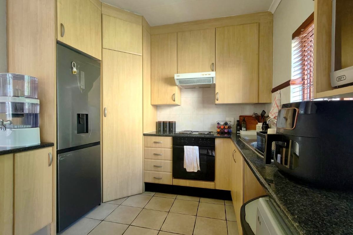 A functional kitchen featuring light wood-finish cabinetry, granite countertops, a built-in oven, hob, and extractor fan, with tiled flooring throughout.