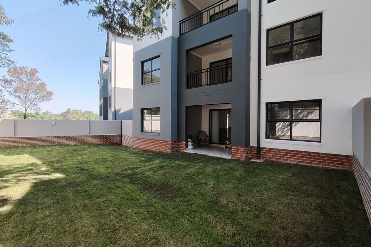 Rear view of a modern apartment building featuring a private ground floor patio, balcony above, and a well-maintained garden area.