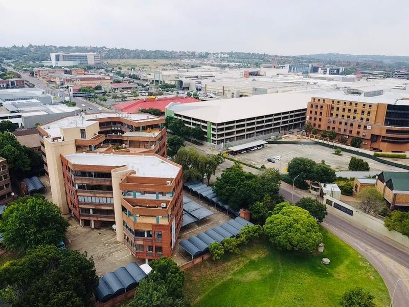 Aerial view of a commercial office complex featuring brick facade buildings, extensive covered parking facilities, and surrounding urban infrastructure.
