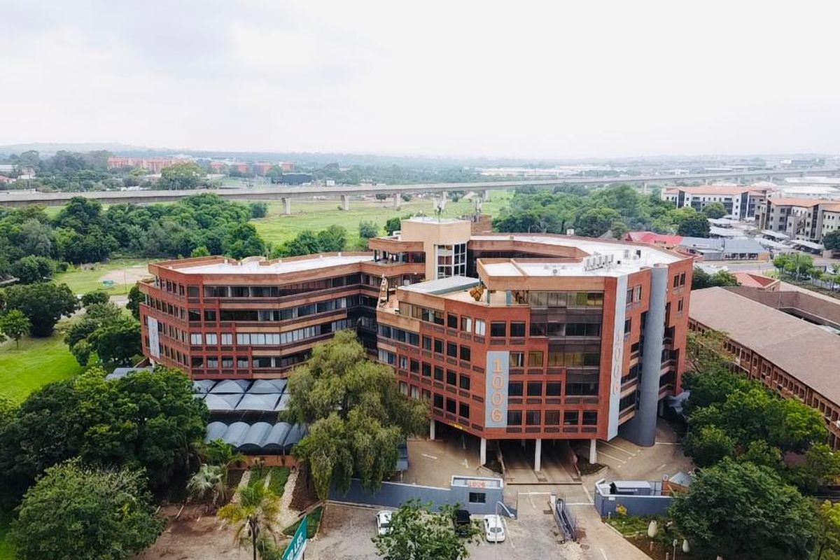 Aerial view of a multi-story commercial office building featuring a brick facade, surrounding landscaped grounds, and dedicated parking facilities.
