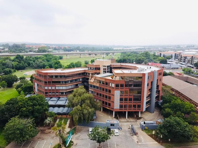 Aerial view of a multi-story commercial office building featuring a brick facade, surrounding landscaped grounds, and dedicated parking facilities.