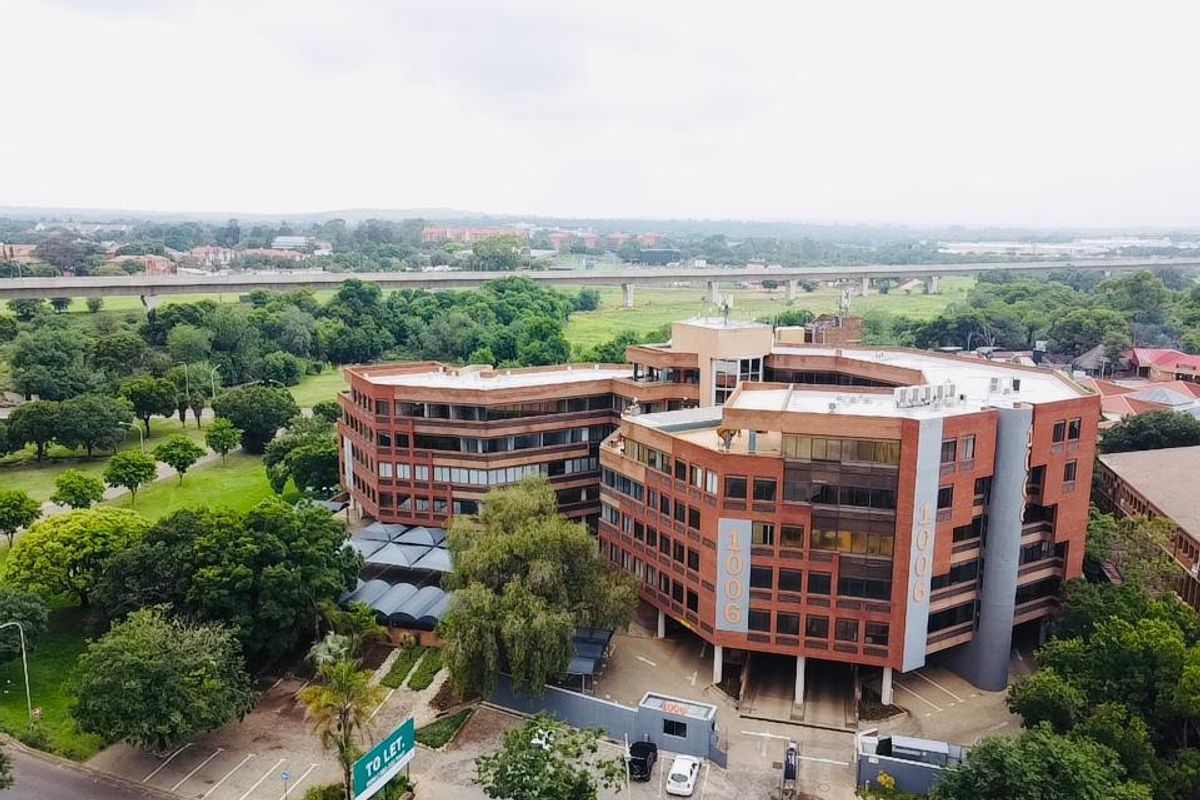 Aerial view of a multi-story commercial office building featuring a brick facade, dedicated parking facilities, and landscaped surroundings in a suburban setting.