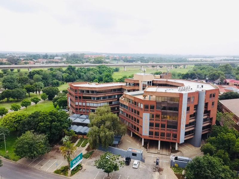 Aerial view of a multi-story commercial office building featuring a brick facade, dedicated parking facilities, and landscaped surroundings in a suburban setting.