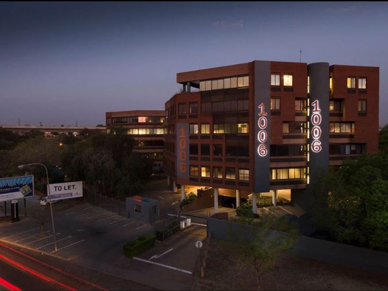 A professional twilight exterior view of a multi-story commercial office building featuring brick facade, prominent signage, and secure on-site parking facilities.