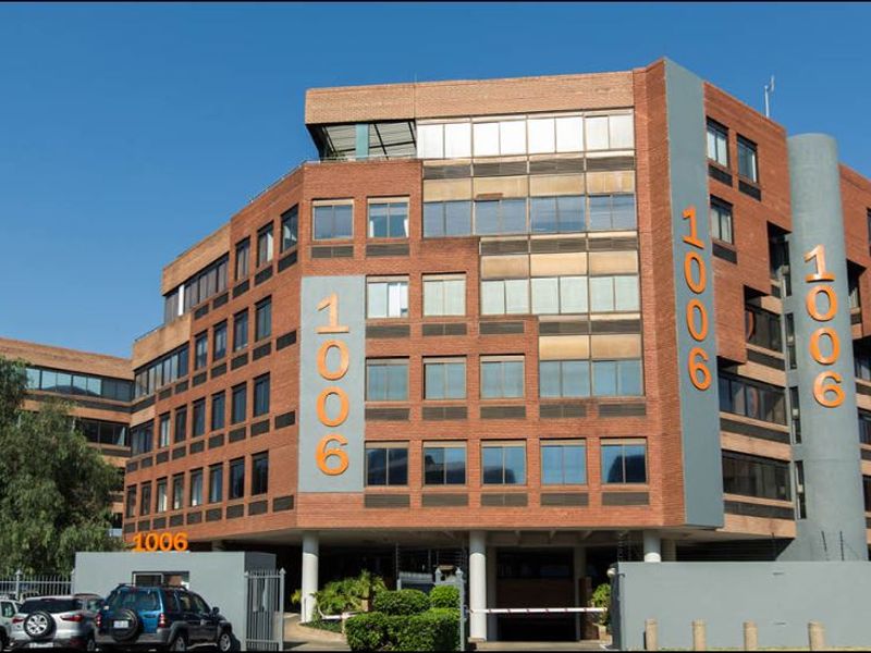 A multi-story commercial office building featuring a brick facade, tinted windows, and a secure gated entrance with on-site parking.