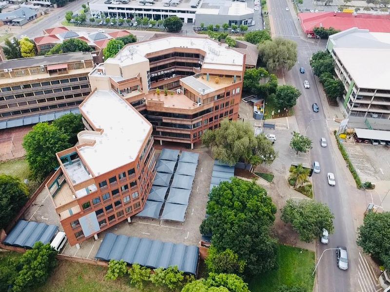 Aerial view of a multi-story commercial office complex featuring brick architecture, flat roofing, and extensive covered parking facilities within an urban setting.