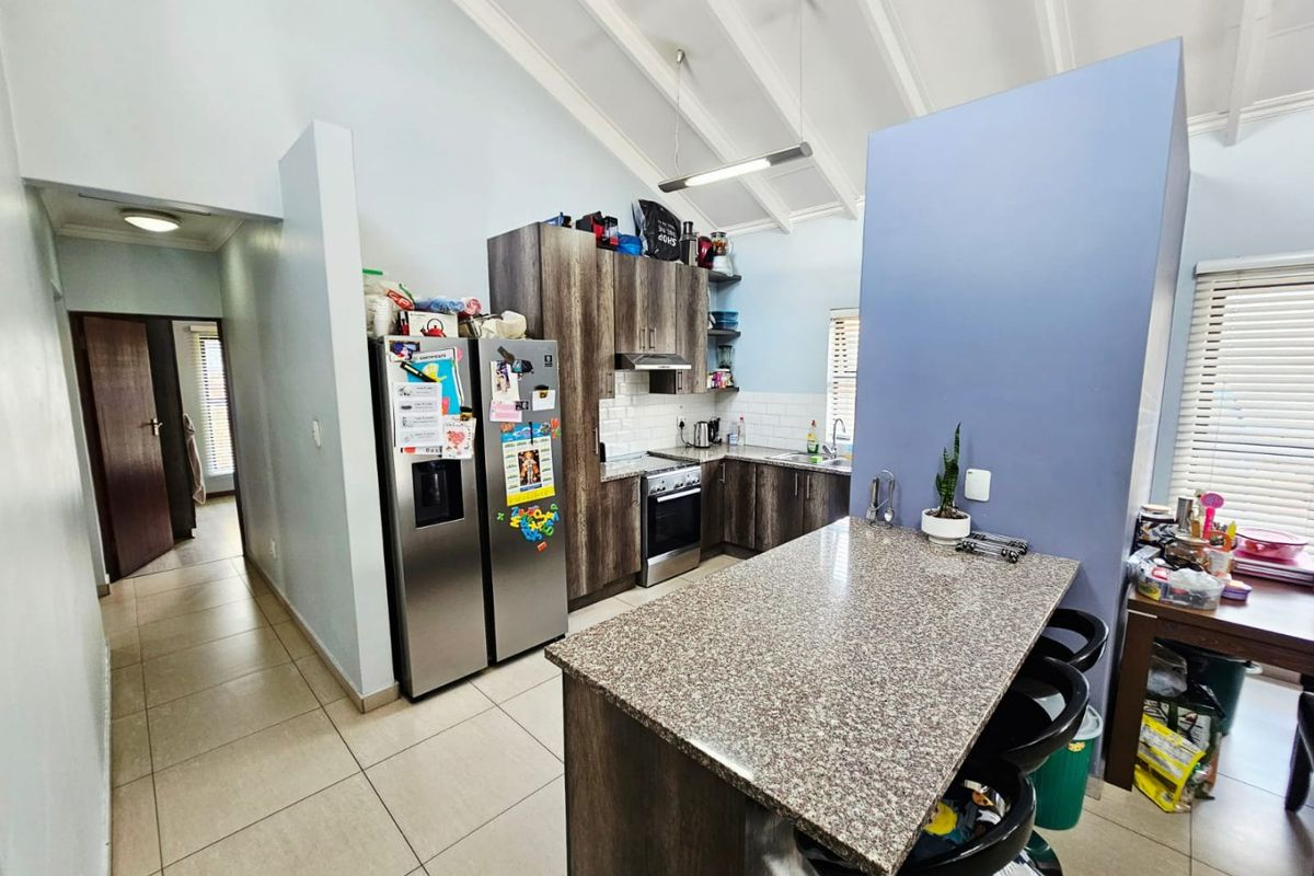 Modern kitchen featuring granite countertops, a central island, tiled flooring, and high vaulted ceilings with exposed beams, offering a functional and open layout.