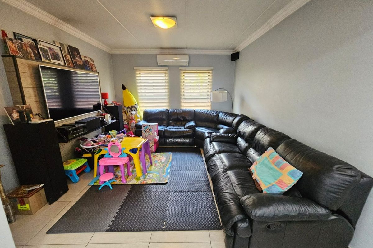 A comfortable living room featuring tiled flooring, a split-system air conditioner, and venetian blinds, providing a functional space for family relaxation.